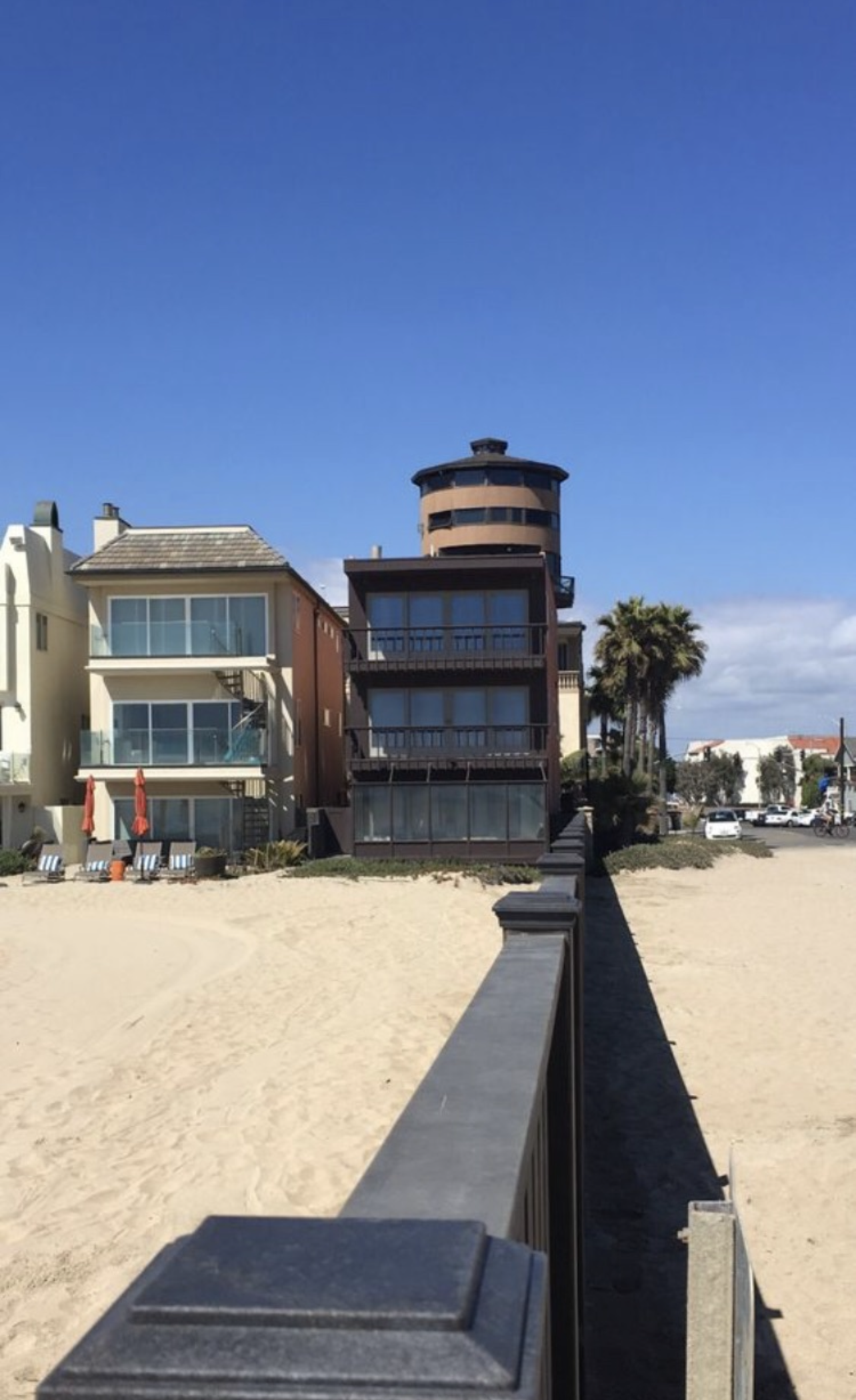 Beachfront homes with the ocean in the background; a dark, low railing in the foreground.
