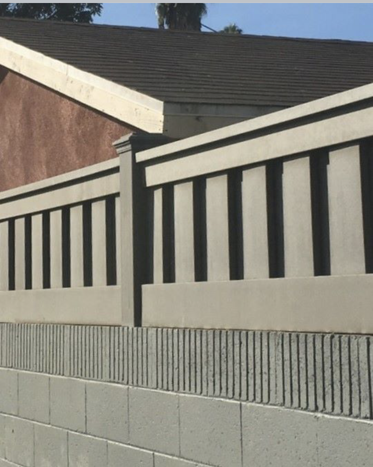 Gray concrete fence with dark vertical slats atop a block wall, next to a brown roof and brick wall.