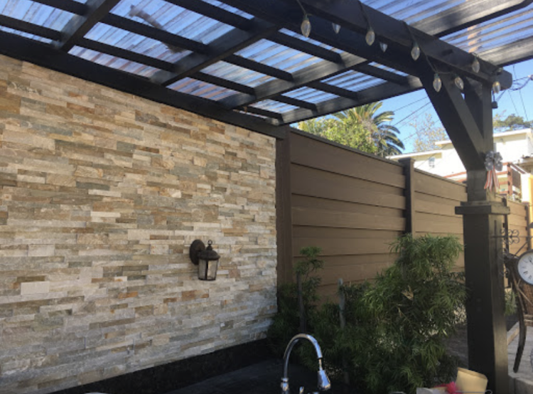 Outdoor patio with stone wall, dark wood pergola, and brown wooden fence.
