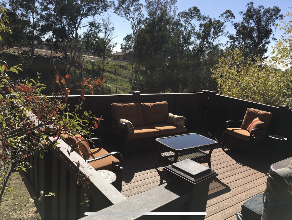 Outdoor deck with brown seating, table, and a view of trees and hills.