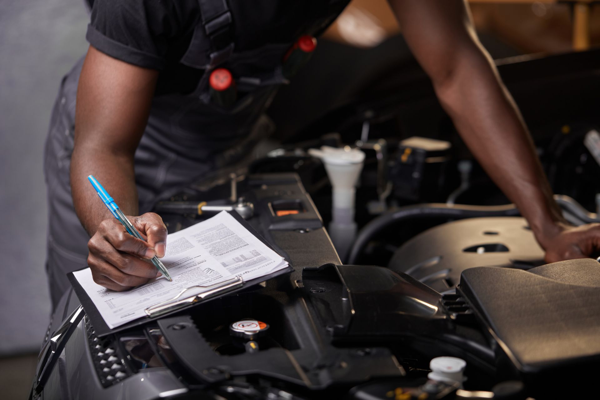 A man is working on a car and writing in a notebook.