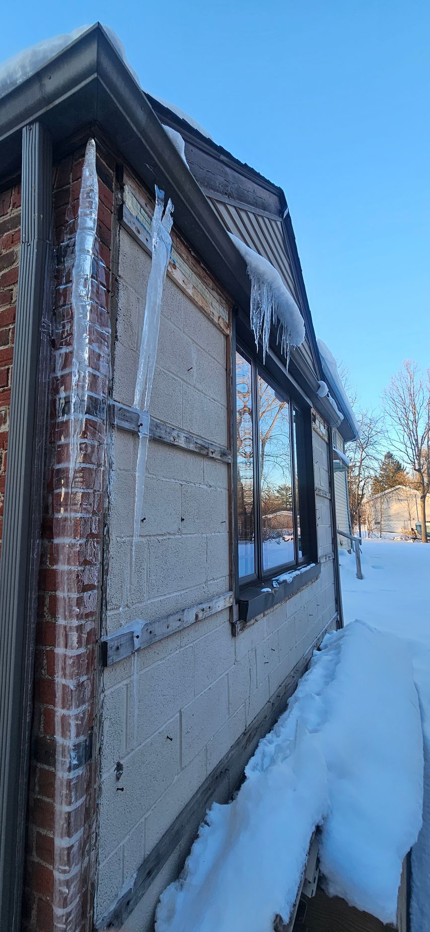 Snow-covered side of a house with a reflective window and icicles on the roofline