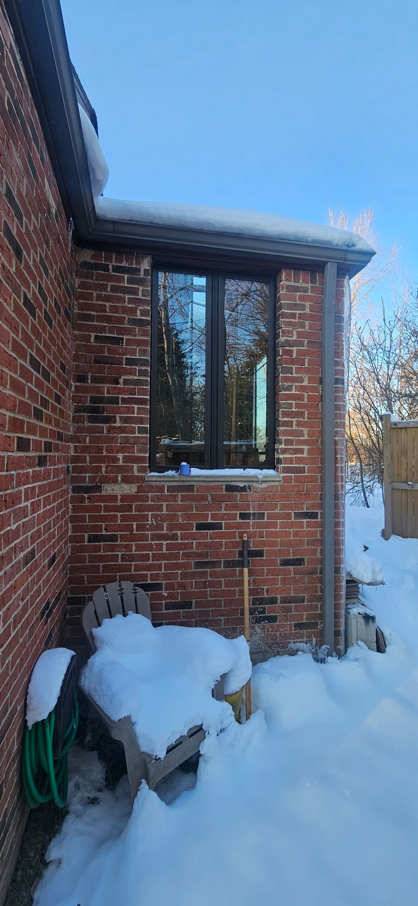 Snow-covered brick house exterior with a window and blue sky above
