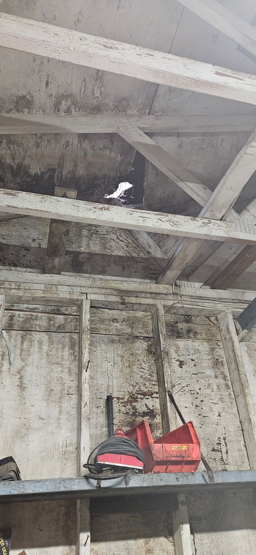 Red life jacket on a dark shelf beneath a weathered, mold-stained ceiling beam.