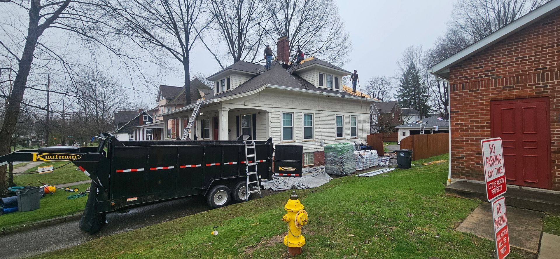 Black dump trailer outside a white house on a rainy day, with a yellow fire hydrant in front.