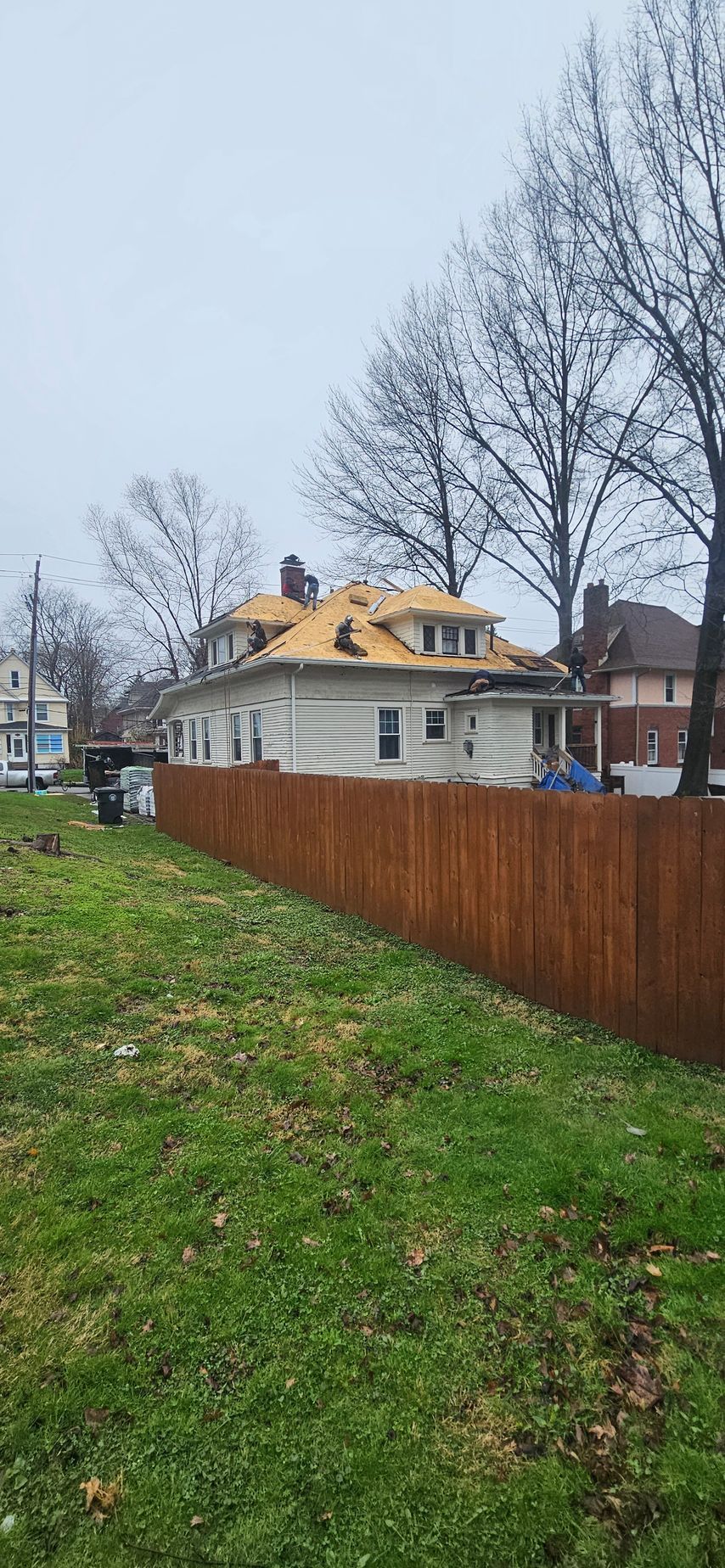 Small white house with a yellow roof behind a brown fence on a cloudy day