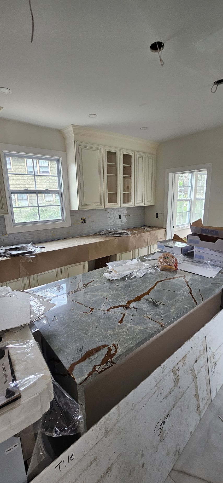 Kitchen under renovation with white cabinets, marble counters, and construction debris on the island