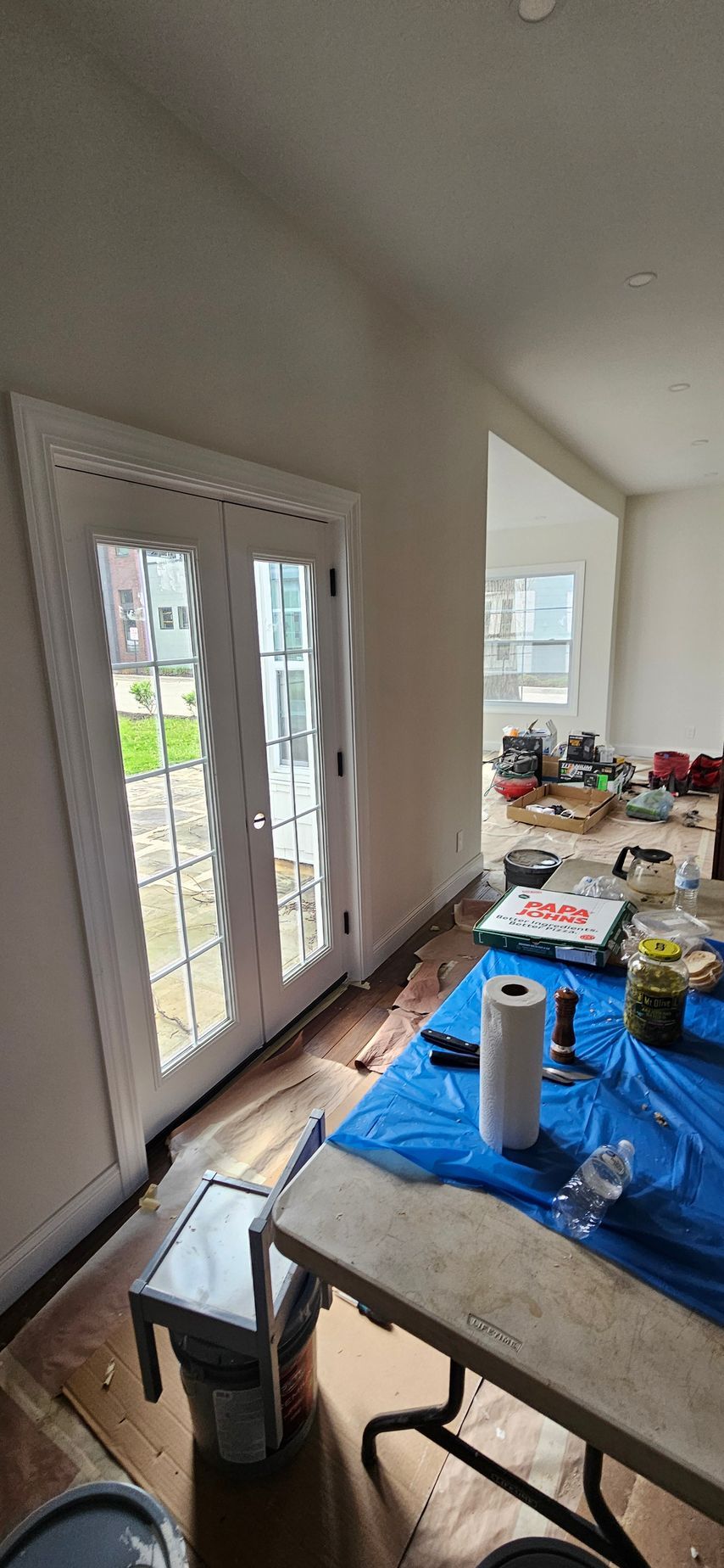 Dining table covered with supplies in a bright room beside glass doors and a window