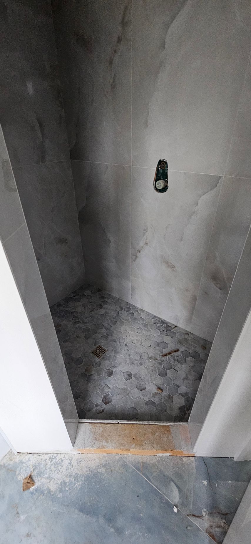 Concrete shower stall with gray walls, dark floor, and a small wall fixture opening