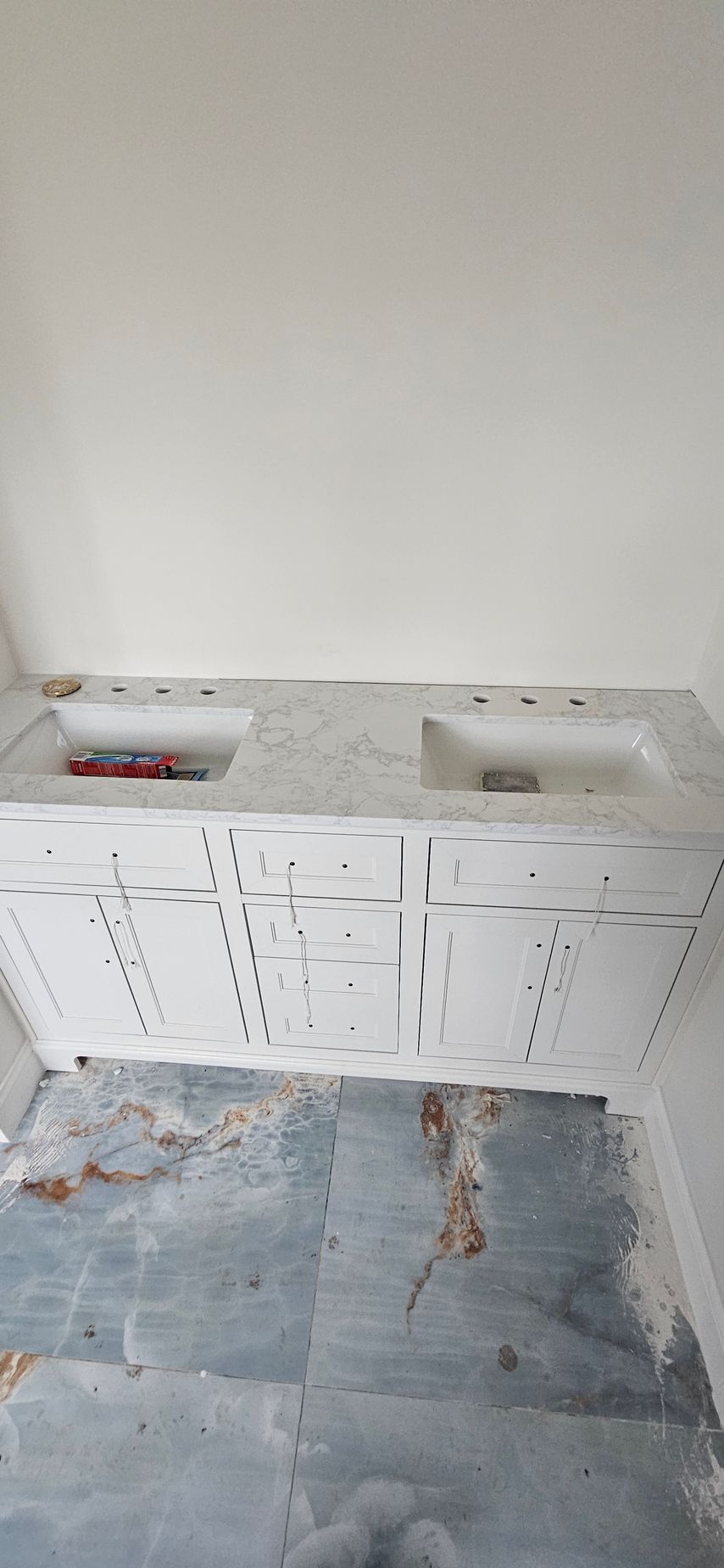 White wall-mounted cabinets and a small shelf above a blue-gray tiled floor in a plain room