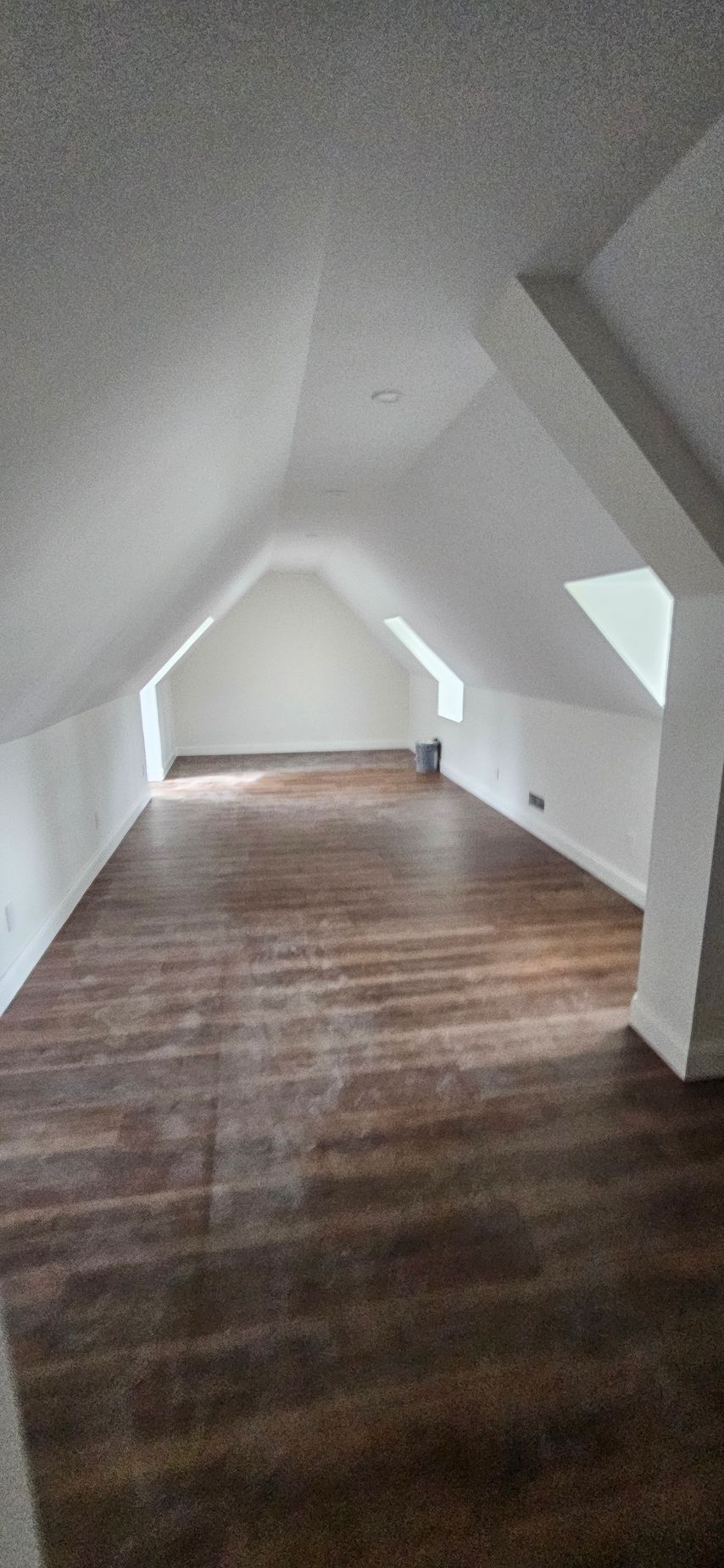 Empty attic room with sloped white ceilings and dark wood floors