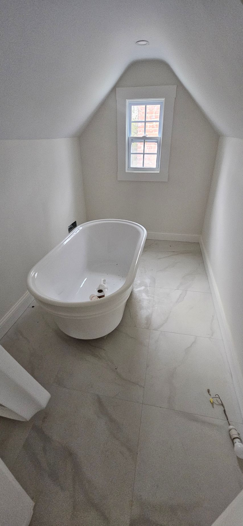 Small attic bathroom with a white clawfoot tub, sloped walls, and a window at the far end.