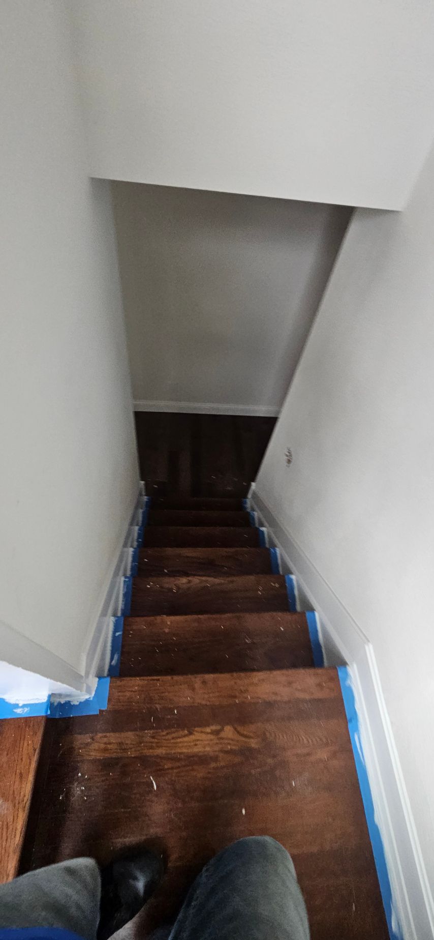 Narrow wooden staircase with blue painter’s tape along the edges, viewed from the top down