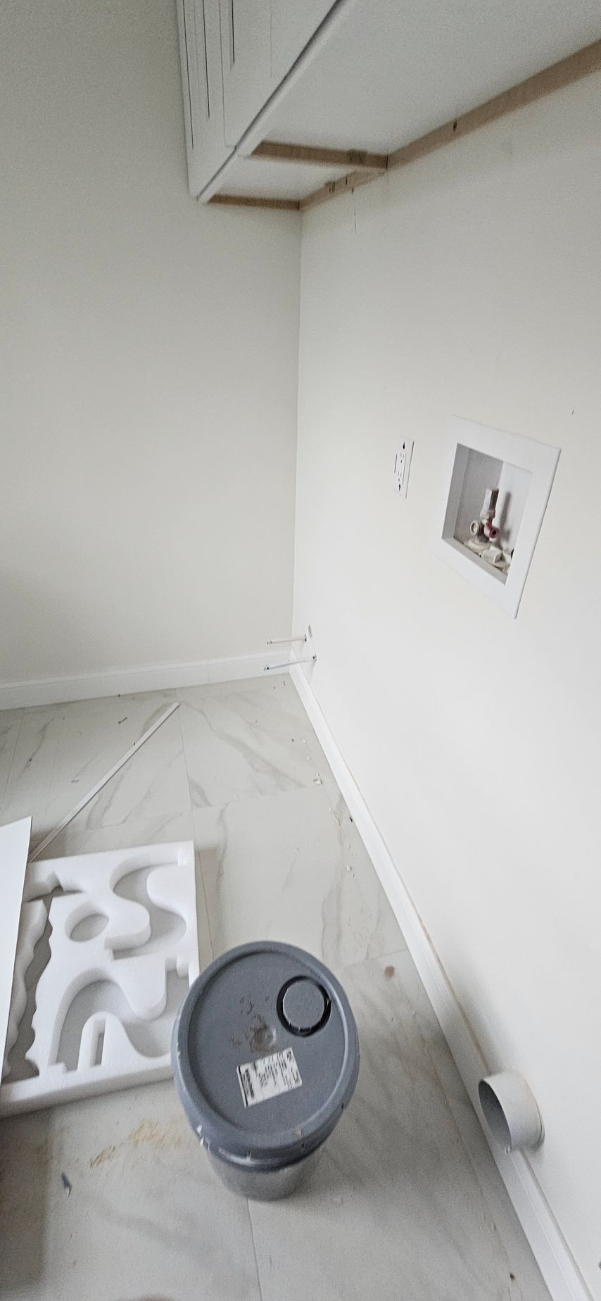 Partially finished white room with a gray bucket and construction materials on the floor
