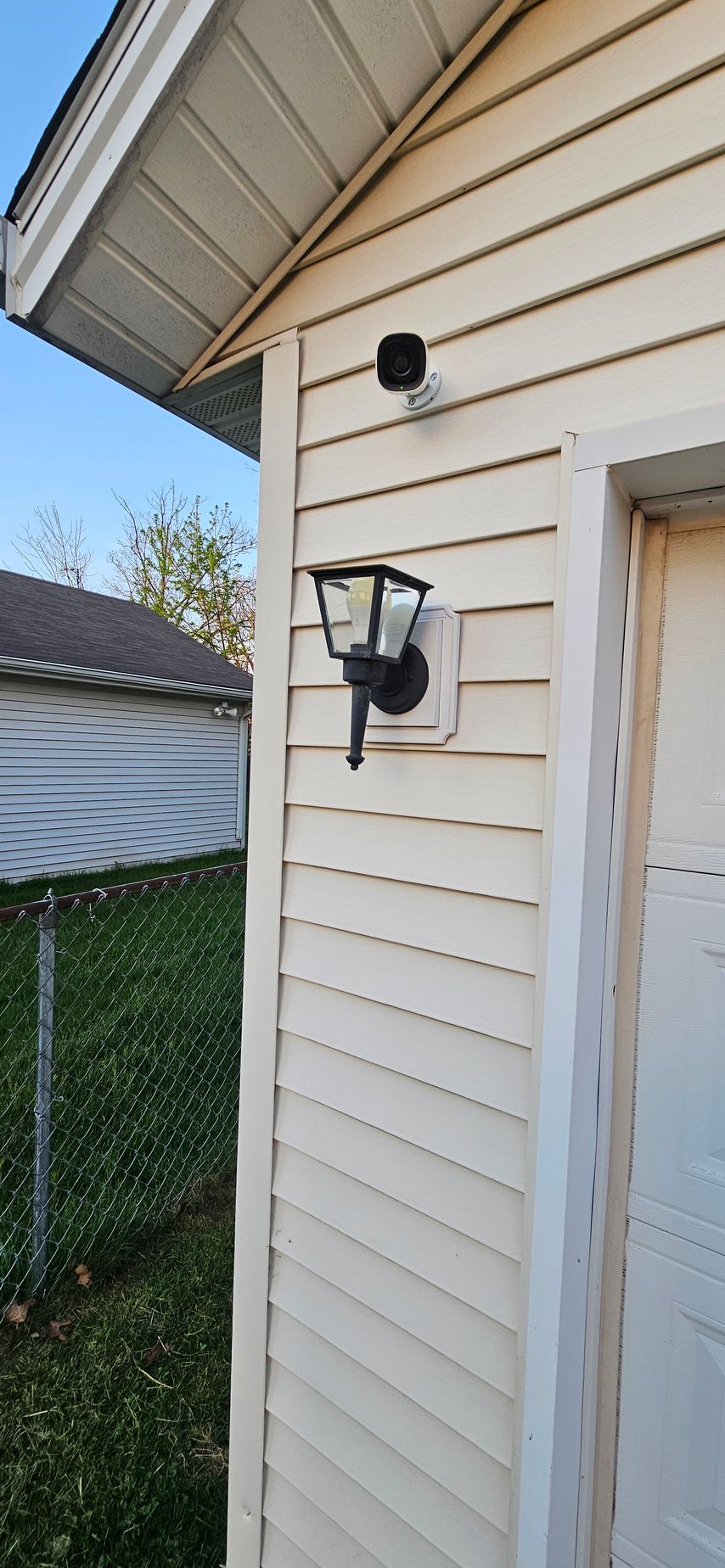 House exterior with beige siding, black wall lanterns, and a fenced yard beside the roofline