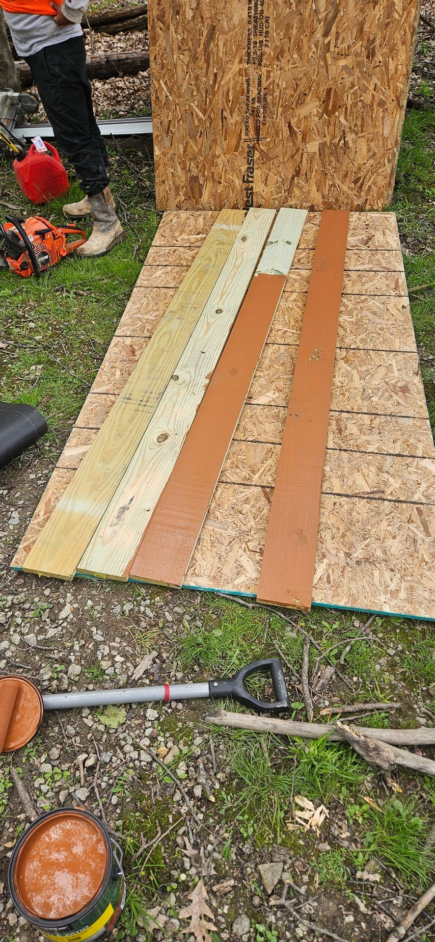 Wooden planks laid on the grass beside a tree stump, with yard tools nearby.