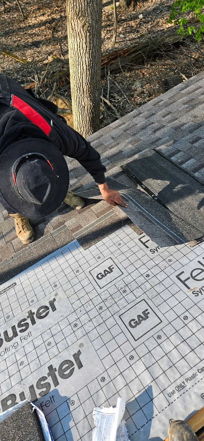 Worker installing roofing underlayment on a sloped roof, using black gloves and tan boots.