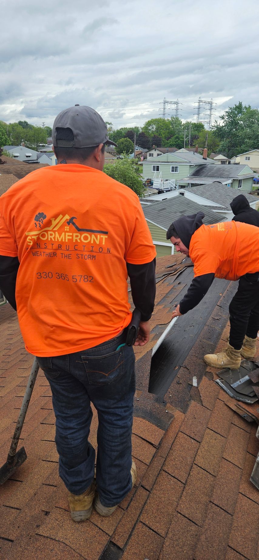 Workers in orange shirts roofing a house with a suburban neighborhood in the background