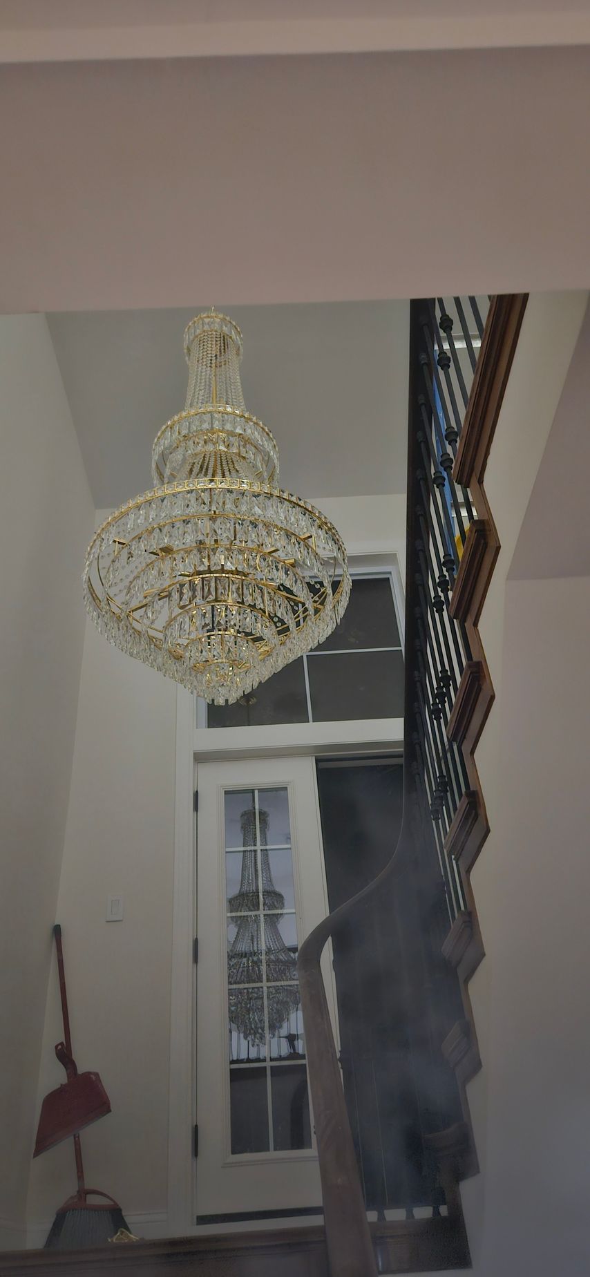 Large crystal chandelier hanging in a narrow hallway beside a window and wall mirror