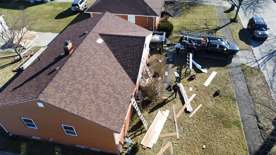 Aerial view of a home renovation project with roofing materials, a ladder, and a truck parked on the lawn.