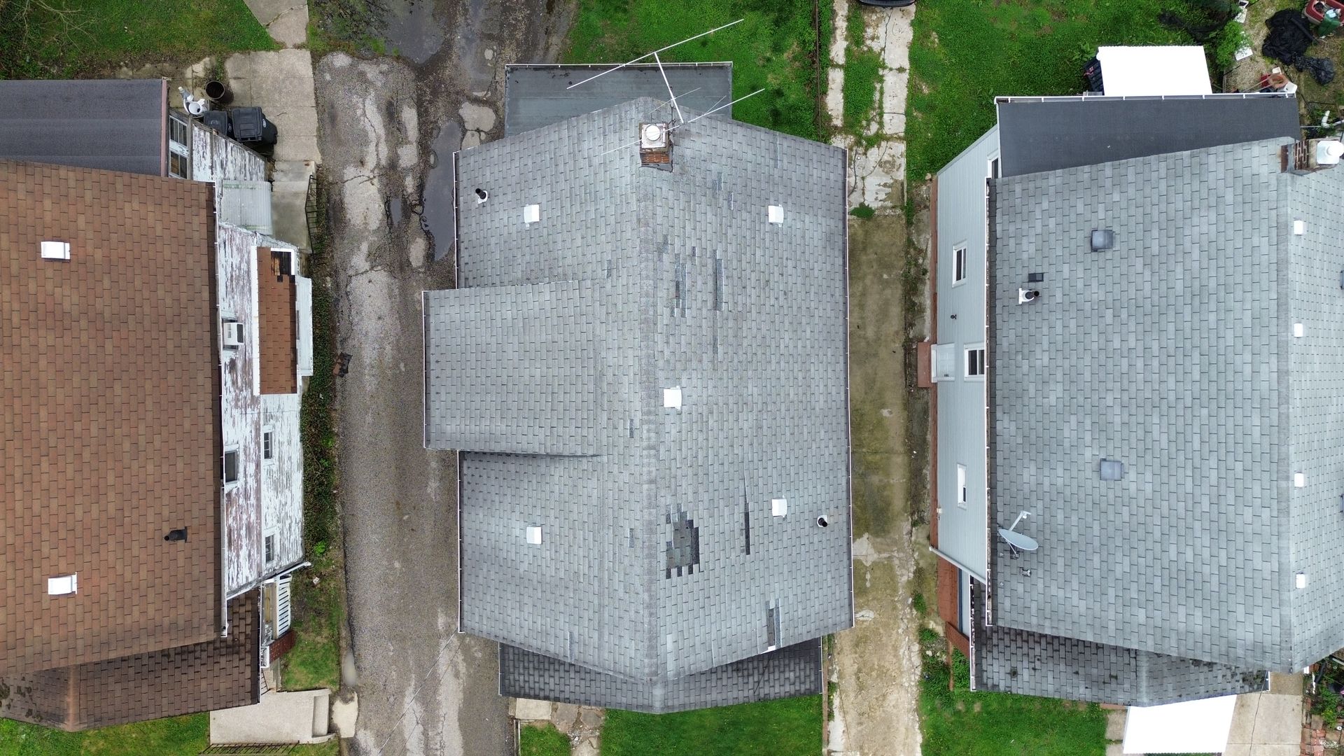 Aerial view of three neighboring houses with gray and brown roofs along narrow driveways.