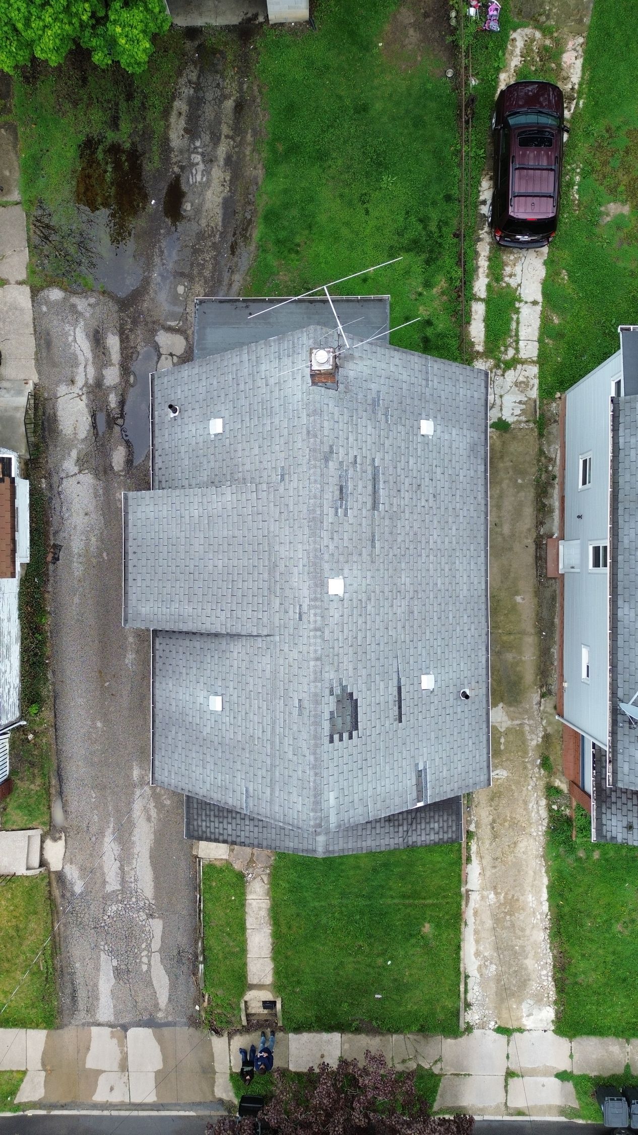 Aerial view of a gray-roofed house with a driveway, lawn, sidewalk, and parked car.