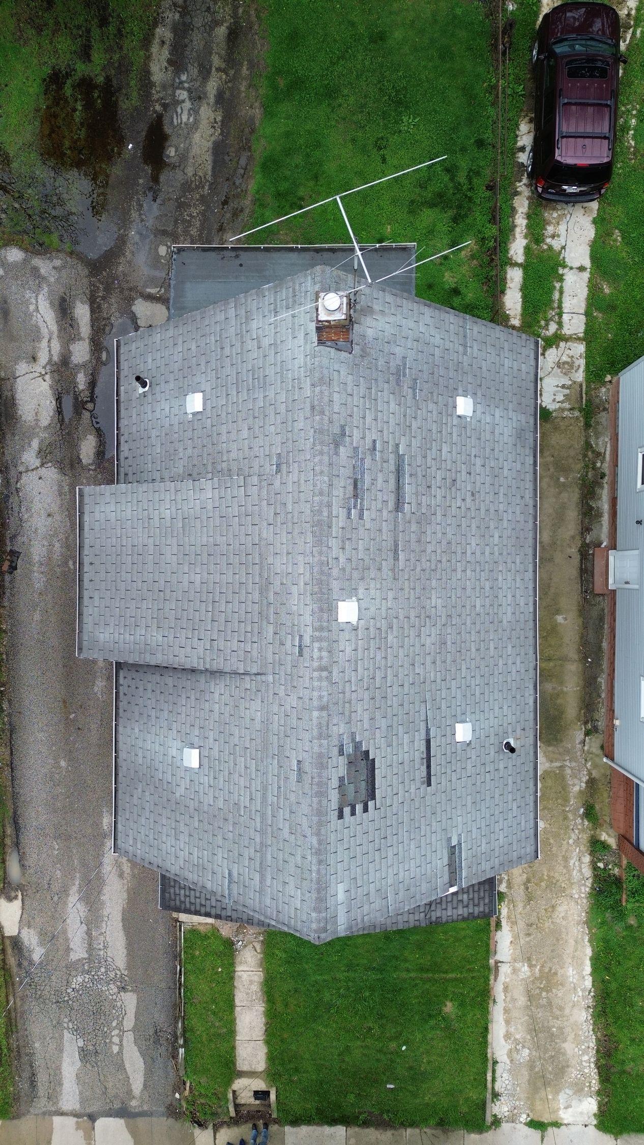 Aerial view of a gray-roofed house with a driveway, lawn, and a parked car nearby.
