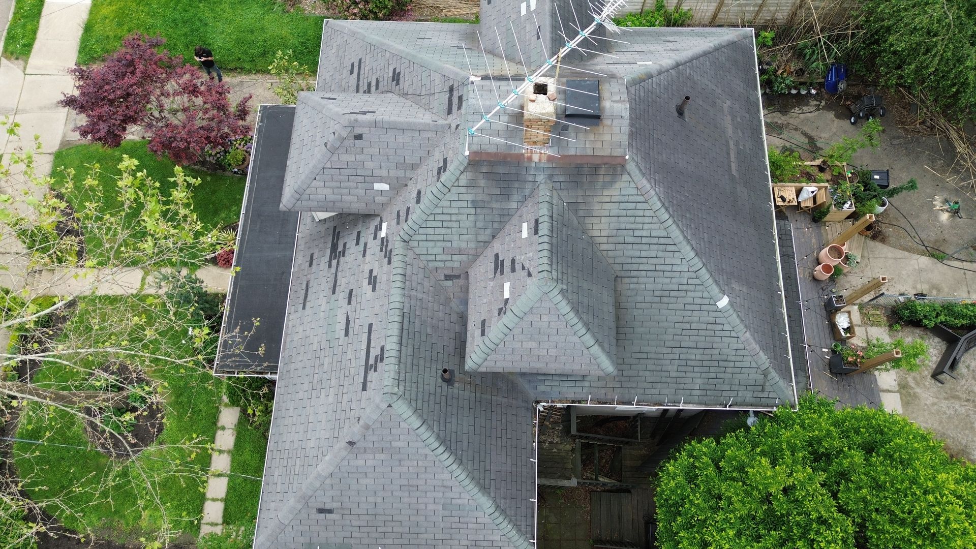 Aerial view of a gray-roofed house with surrounding green yard and trees