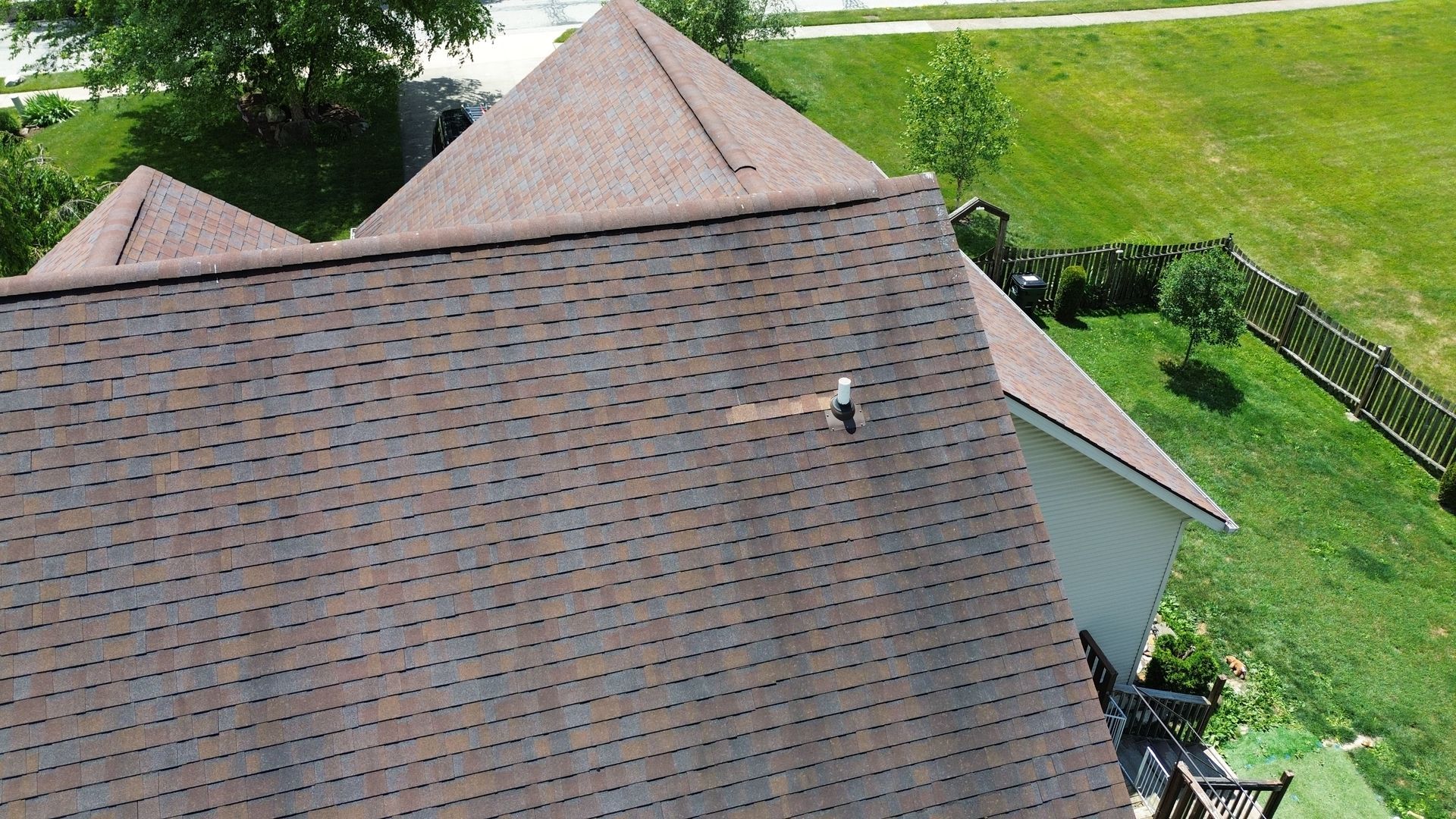 Aerial view of a brown shingled roof beside a green lawn and fence.