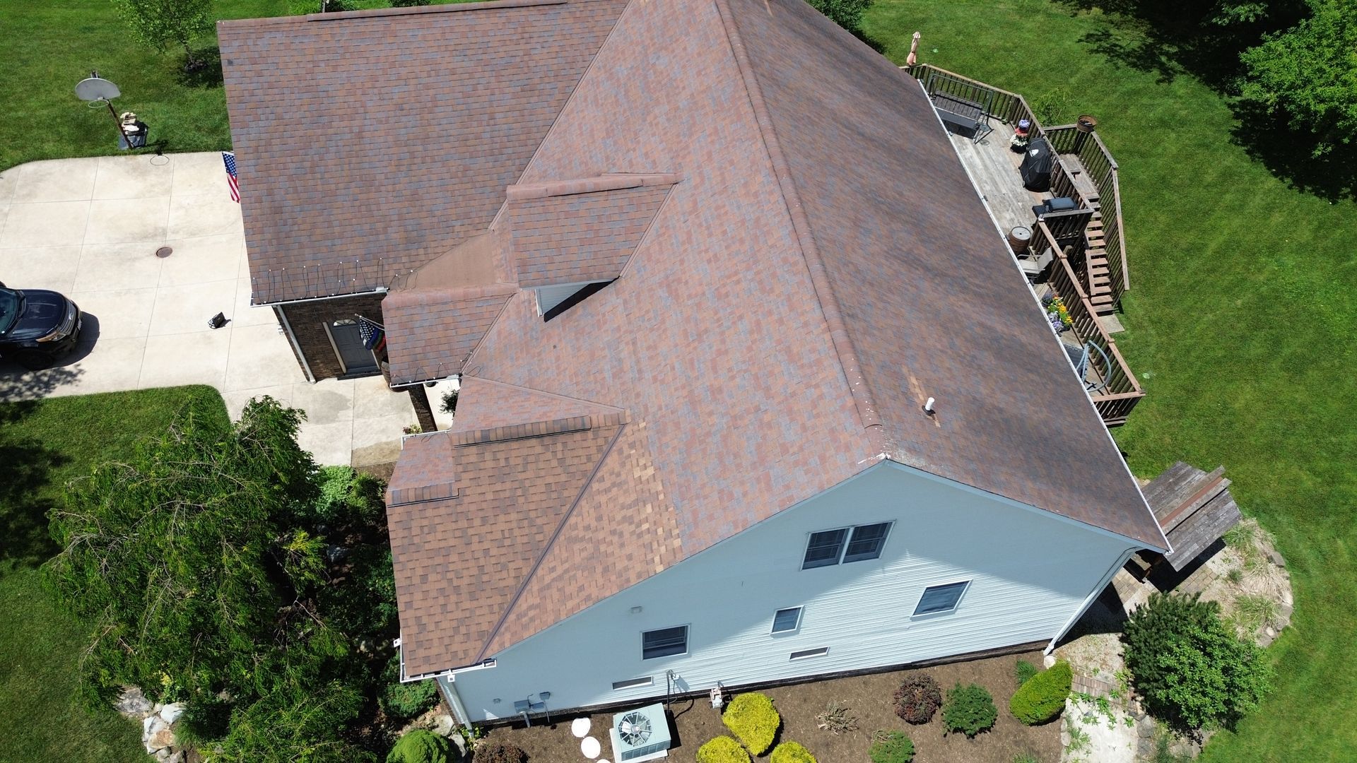 Aerial view of a house with a brown roof, light blue siding, driveway, and green lawn.