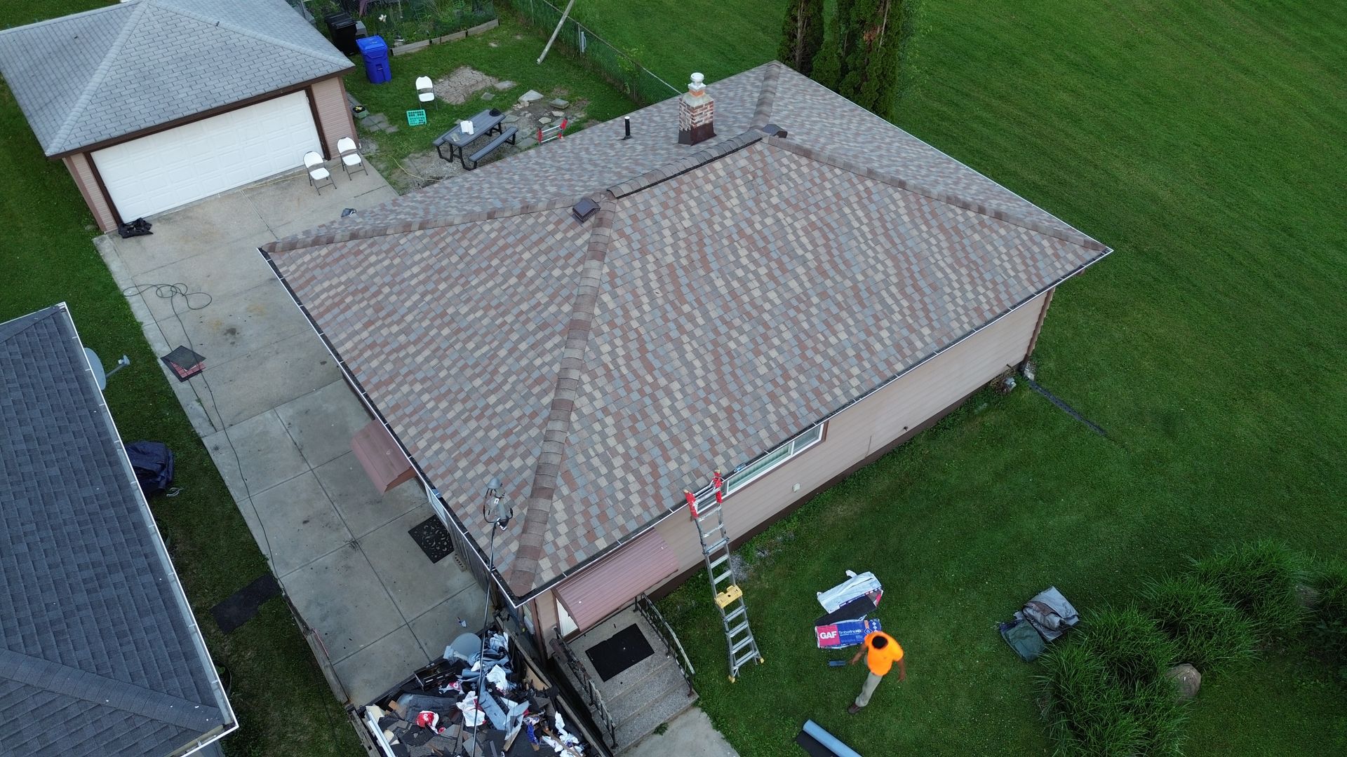 Aerial view of a house roof with workers and equipment in the yard during repairs