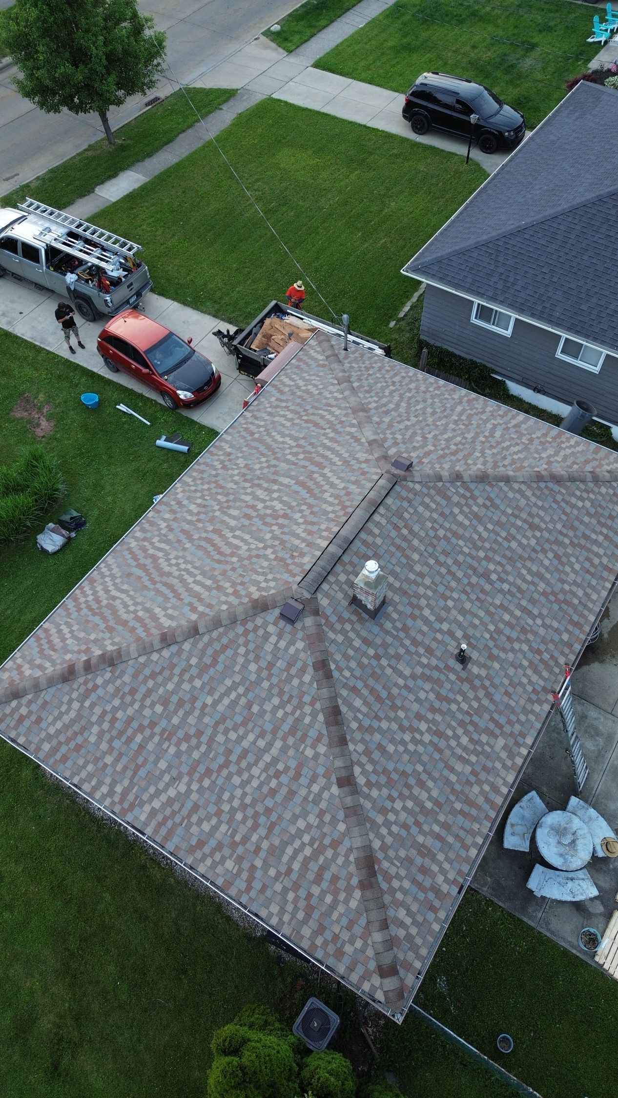 Aerial view of a suburban house with a driveway, parked vehicles, and a person near the garage.