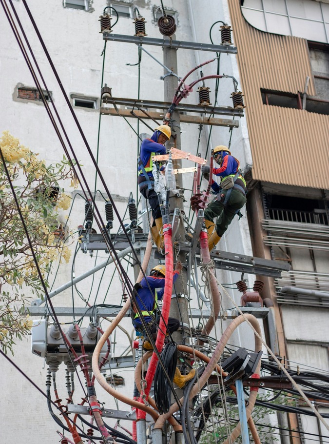 Utility workers on a power pole handling cables and equipment on a street corner.
