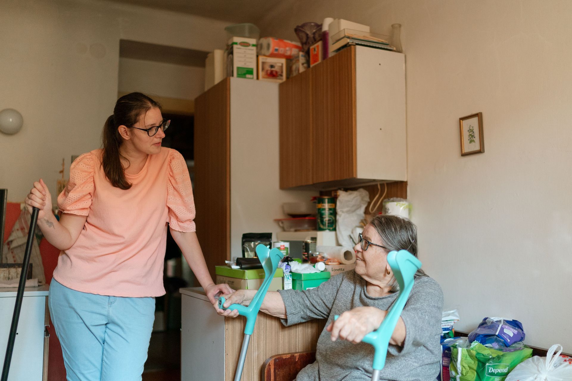 Two people talking in a kitchen, one standing and one seated in a high chair.