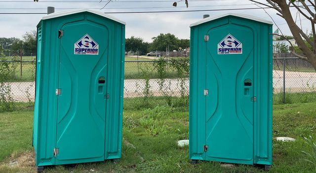 Two portable toilets are next to each other in front of a stone wall