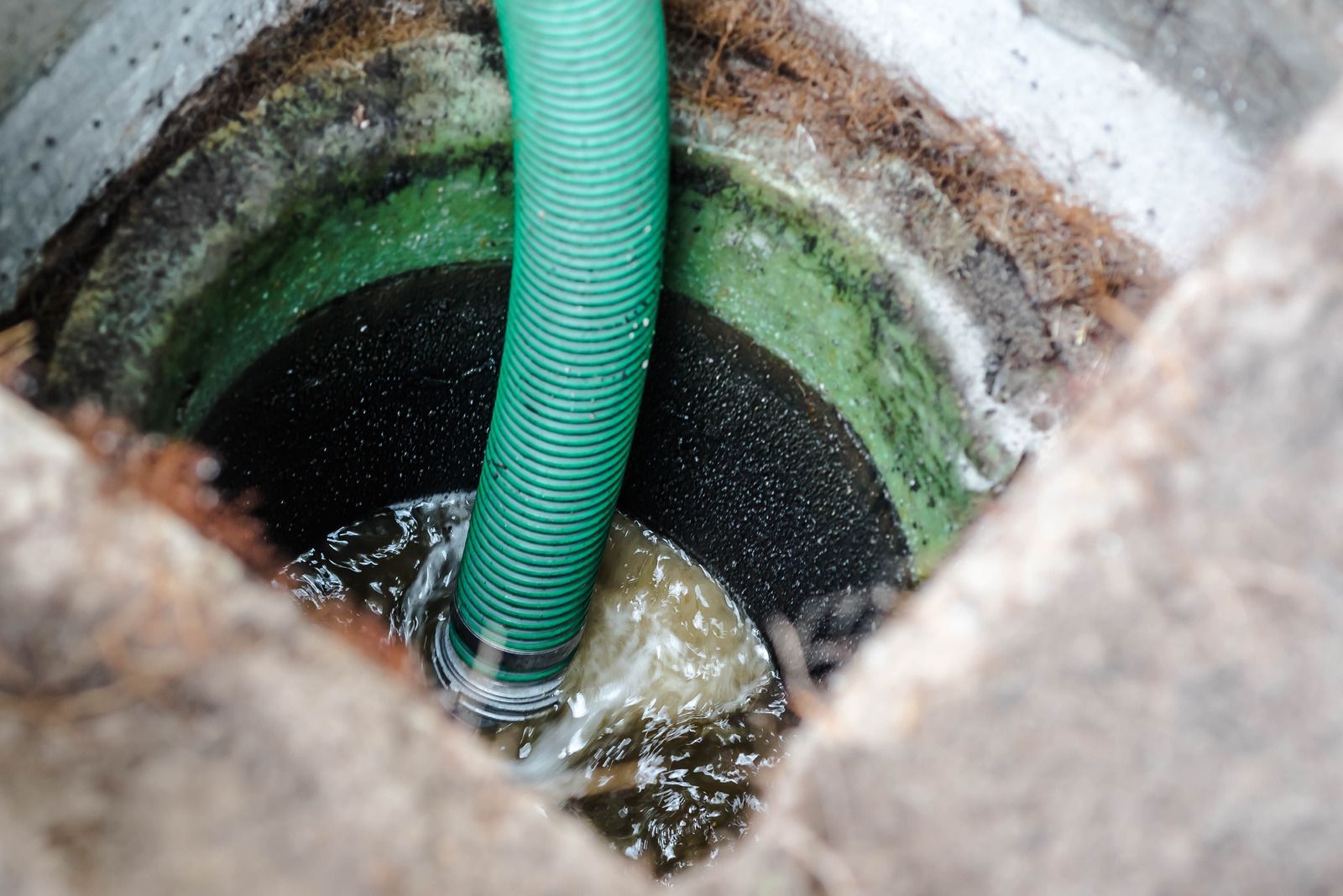 Green hose pumping water from a dark, circular well.