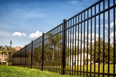 Black metal fence beside a green lawn under a blue sky with clouds Black metal fence beside a green lawn under a blue sky with clouds