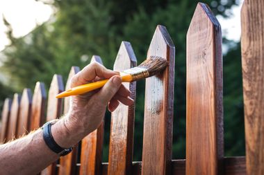 Hand painting a brown wooden fence with a brush outdoors Hand painting a brown wooden fence with a brush outdoors