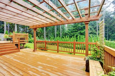 Wooden deck and pergola with railing overlooking a lush green garden and trees Wooden deck and pergola with railing overlooking a lush green garden and trees