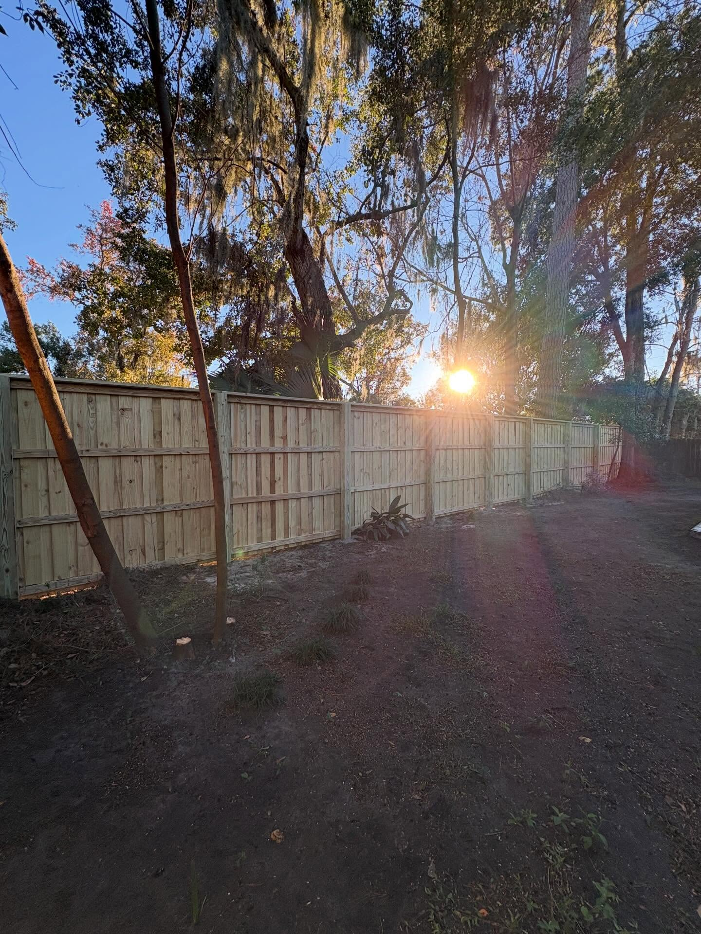 Gray metal fence beside a driveway, with a house and flowers in the background.