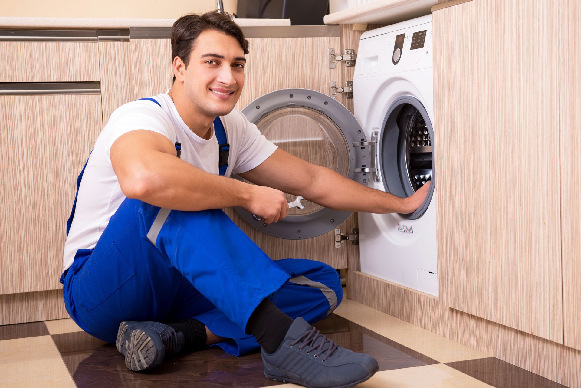 A man is sitting on the floor fixing a washing machine.