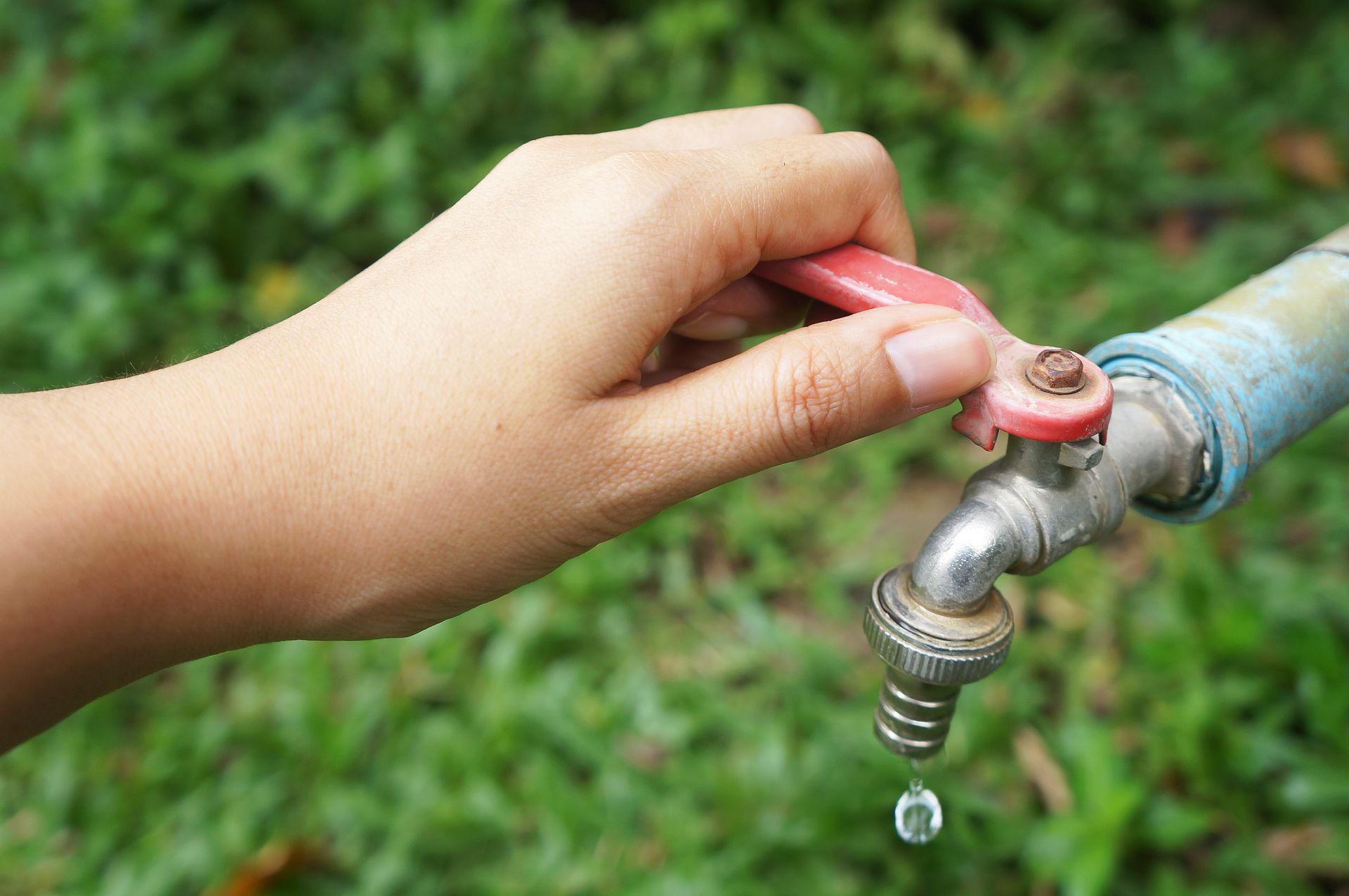 A person is opening a faucet with a red handle.