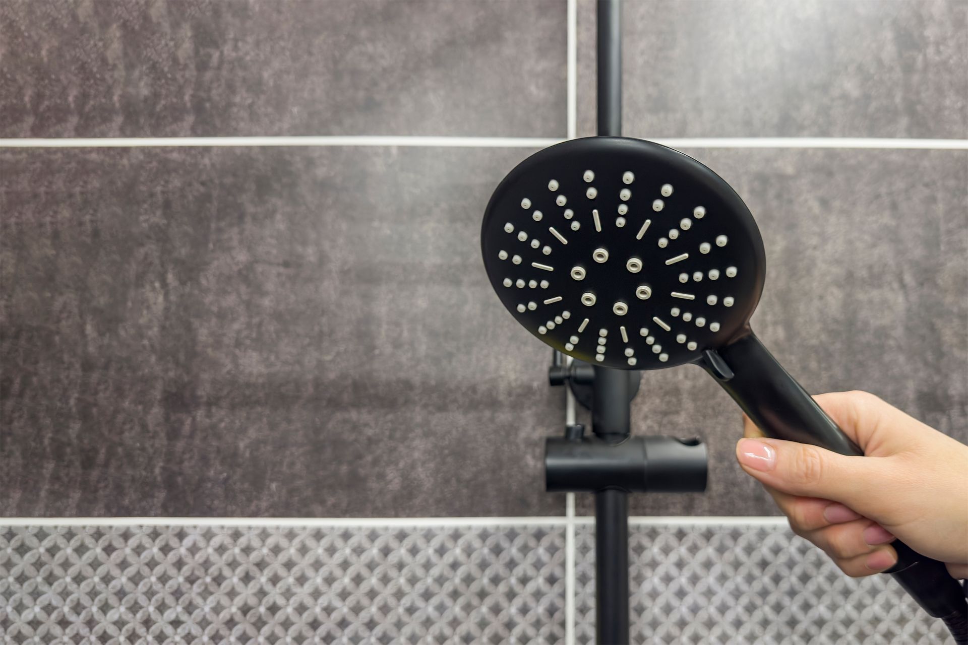 A person is holding a black shower head in a bathroom.