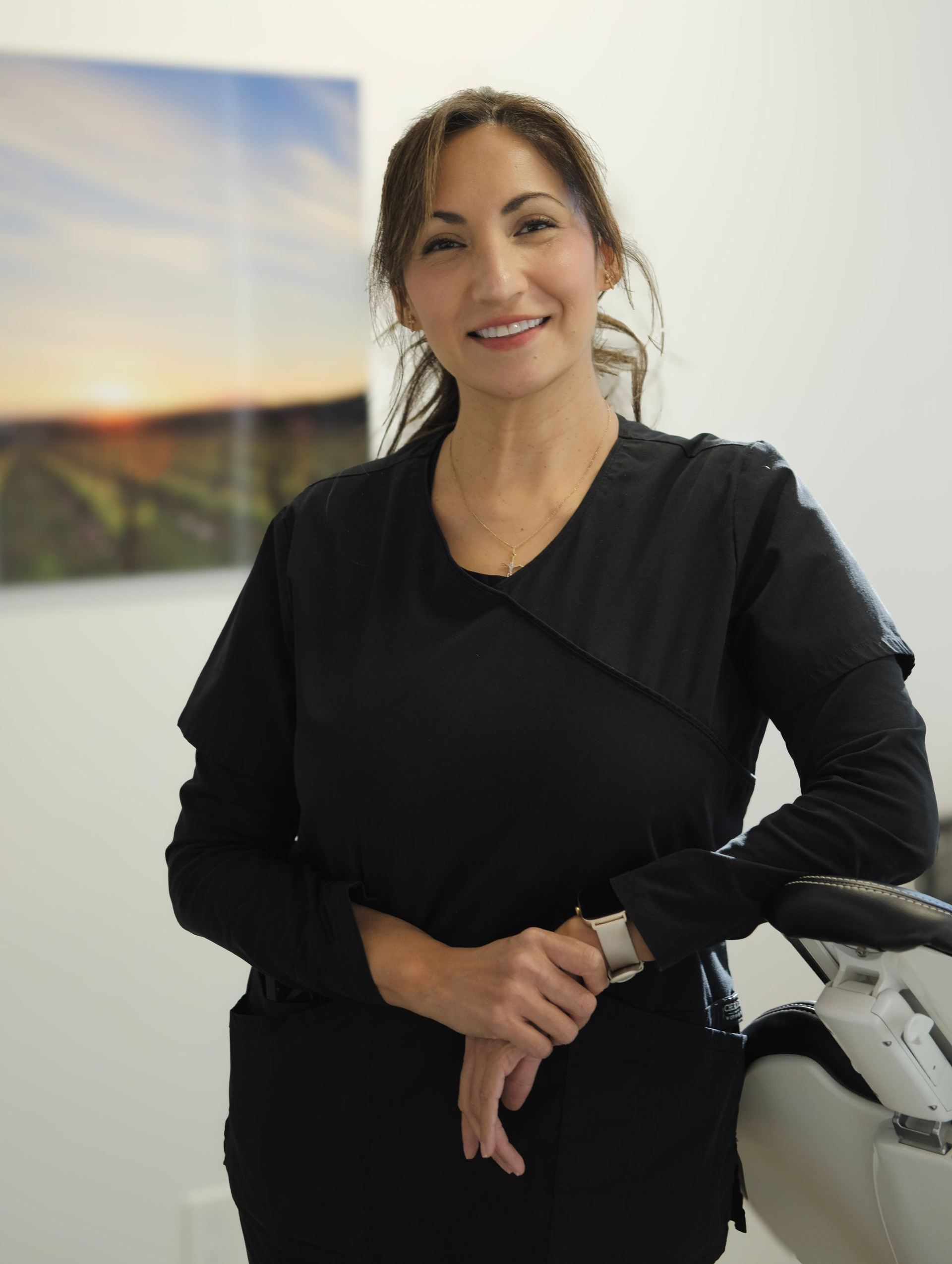 Woman in black scrubs smiles, leaning on medical equipment. Modern office setting, landscape art.