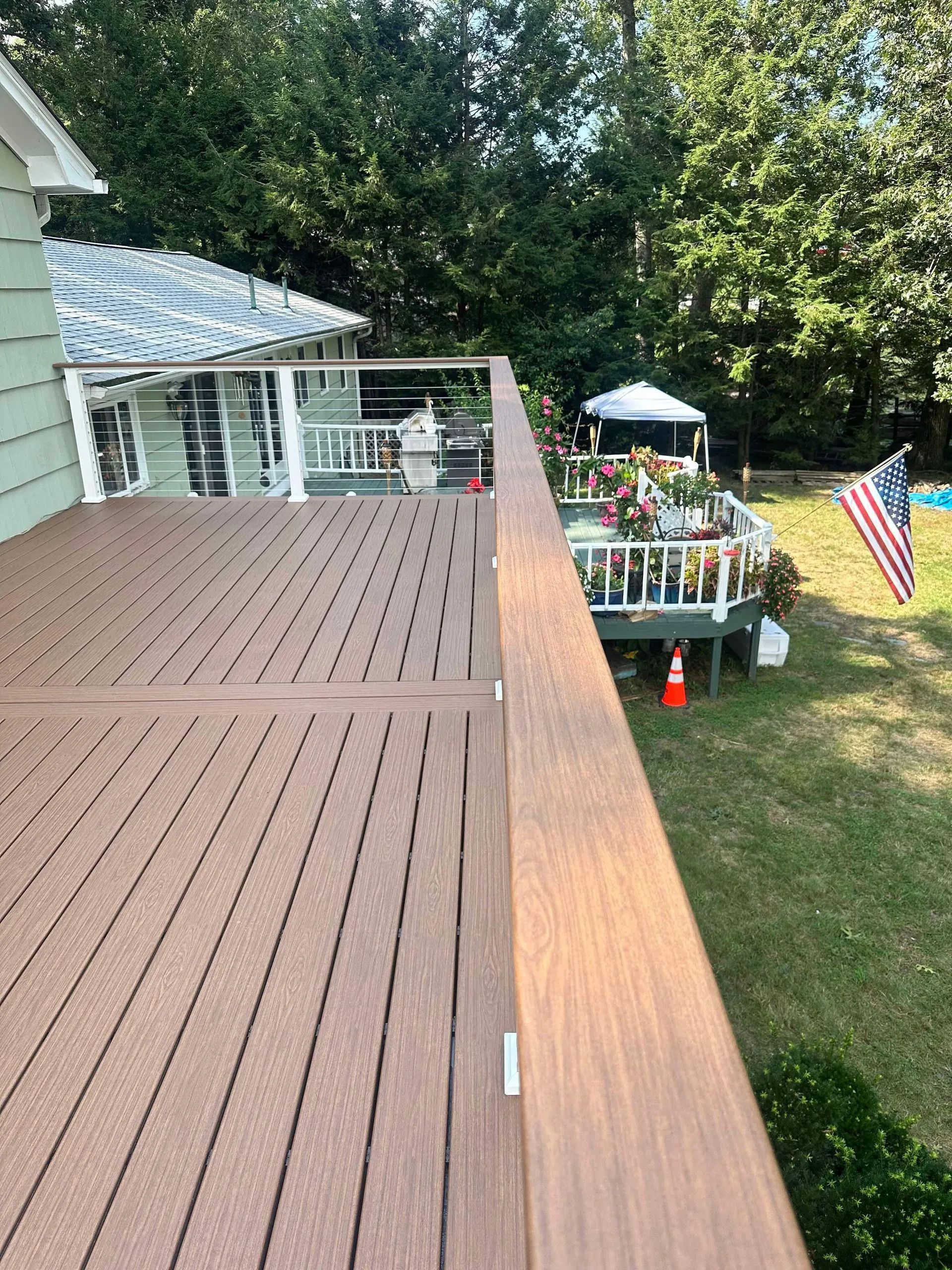 Wooden deck overlooking a backyard with a small garden area, umbrella, and American flag.