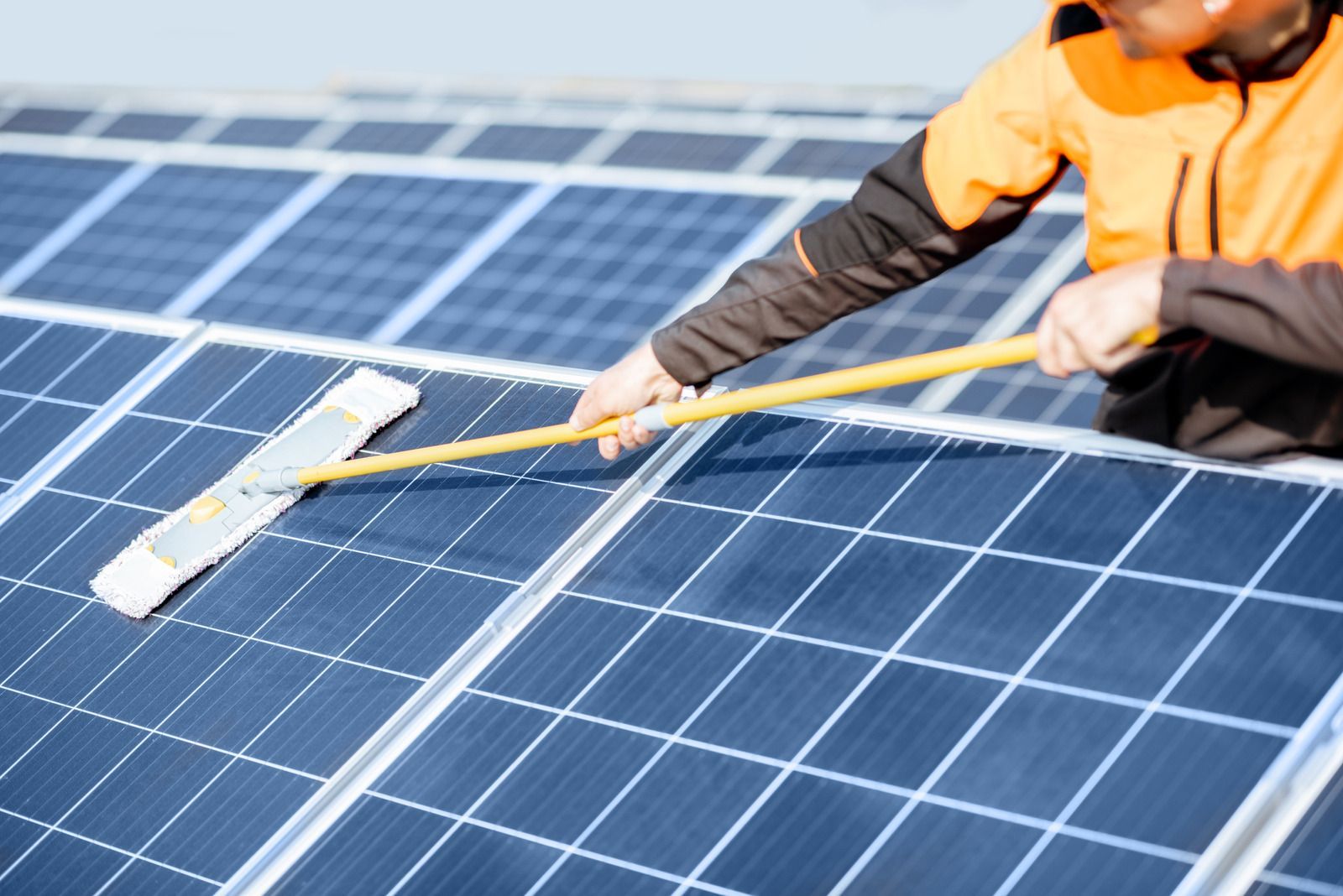 A man is cleaning solar panels with a mop.