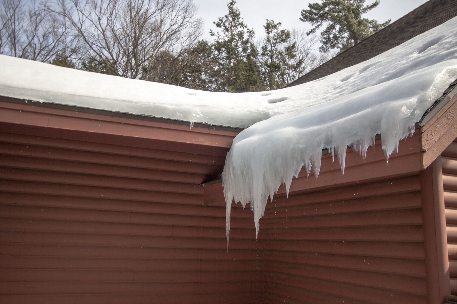 Snow-covered roof edge with large hanging icicles on a brown house exterior