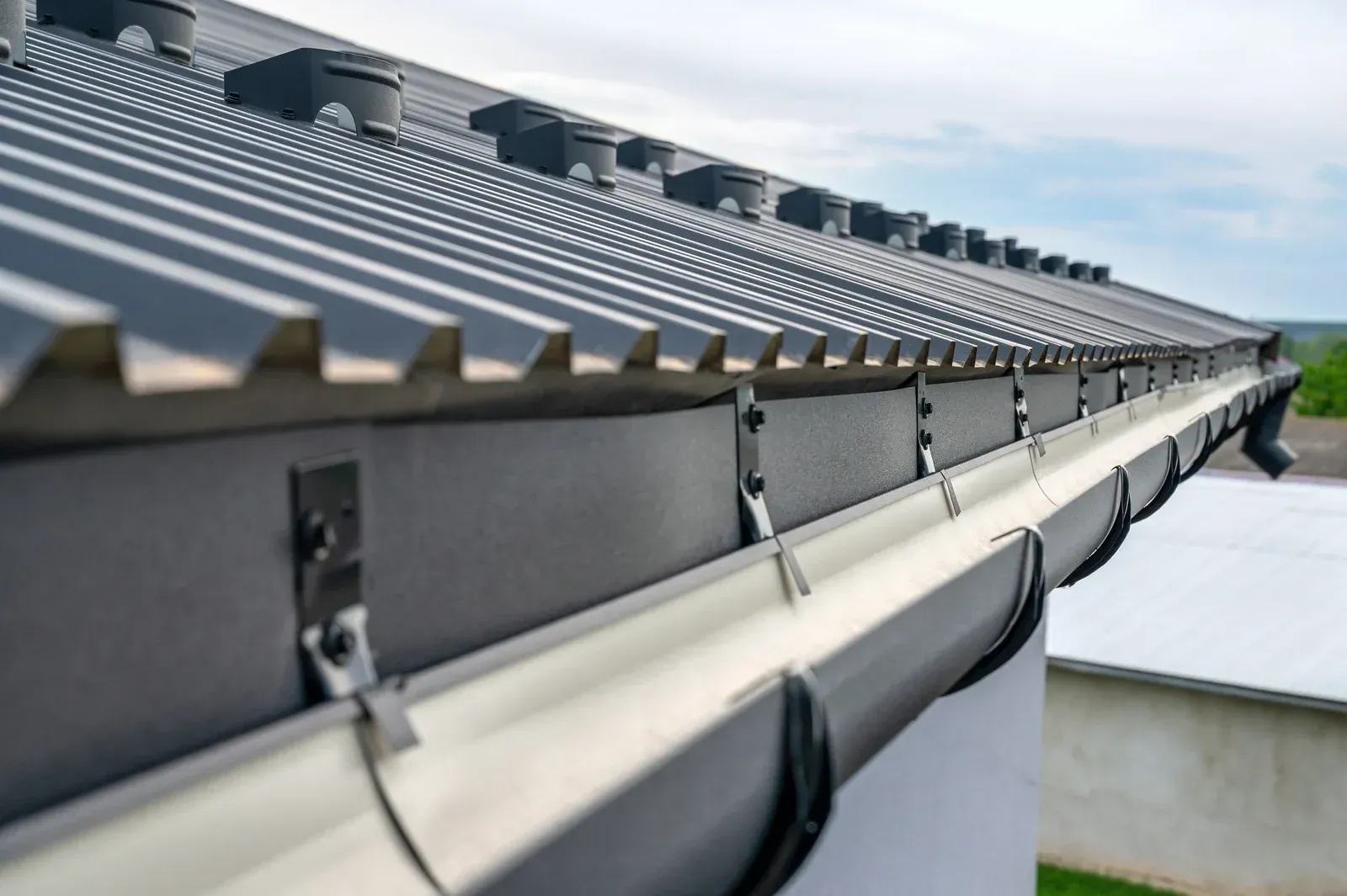Close-up of a metal gutter system along a corrugated roof under a cloudy sky