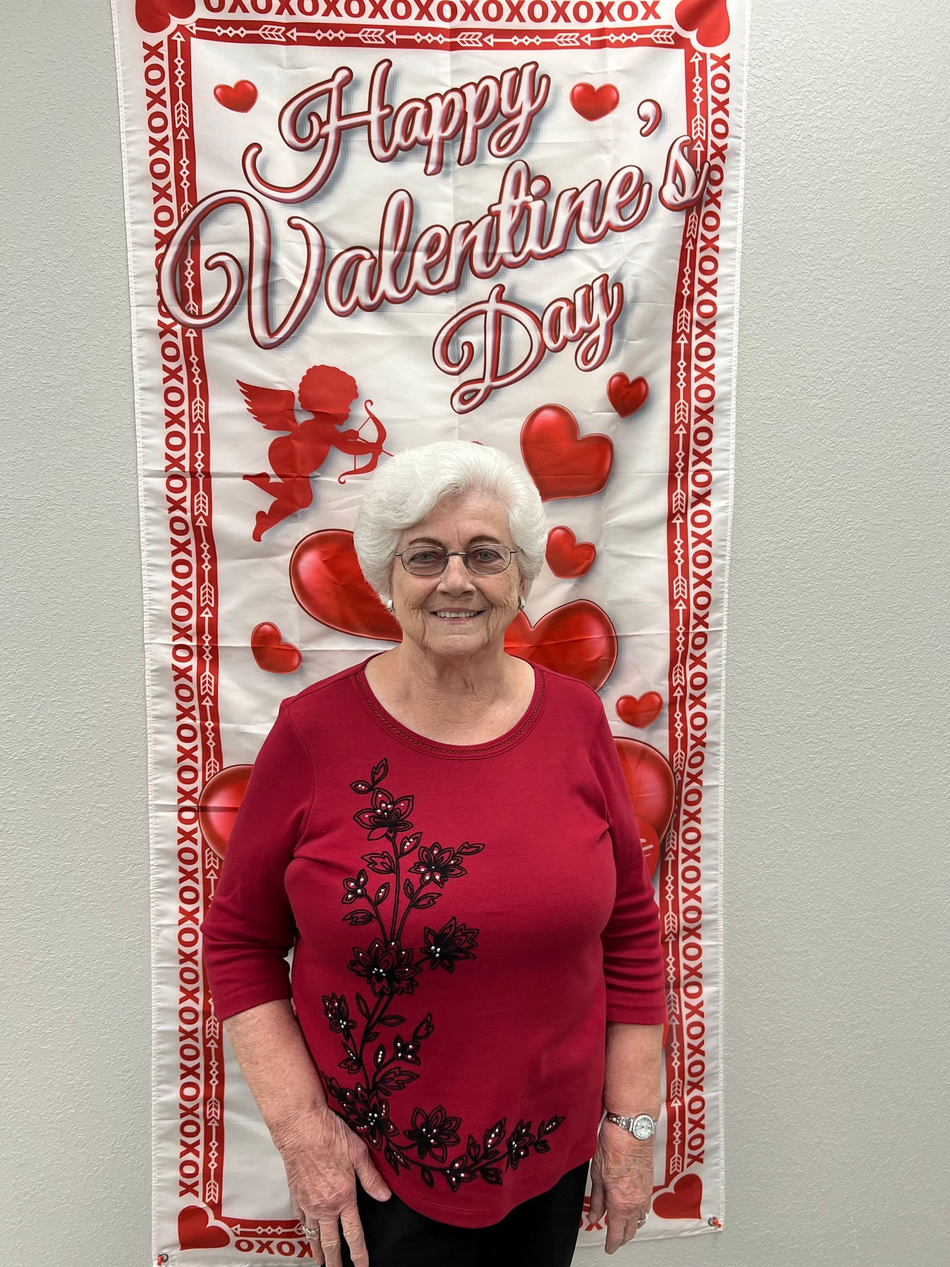 Woman in red sweater smiles in front of a Valentine's Day banner.
