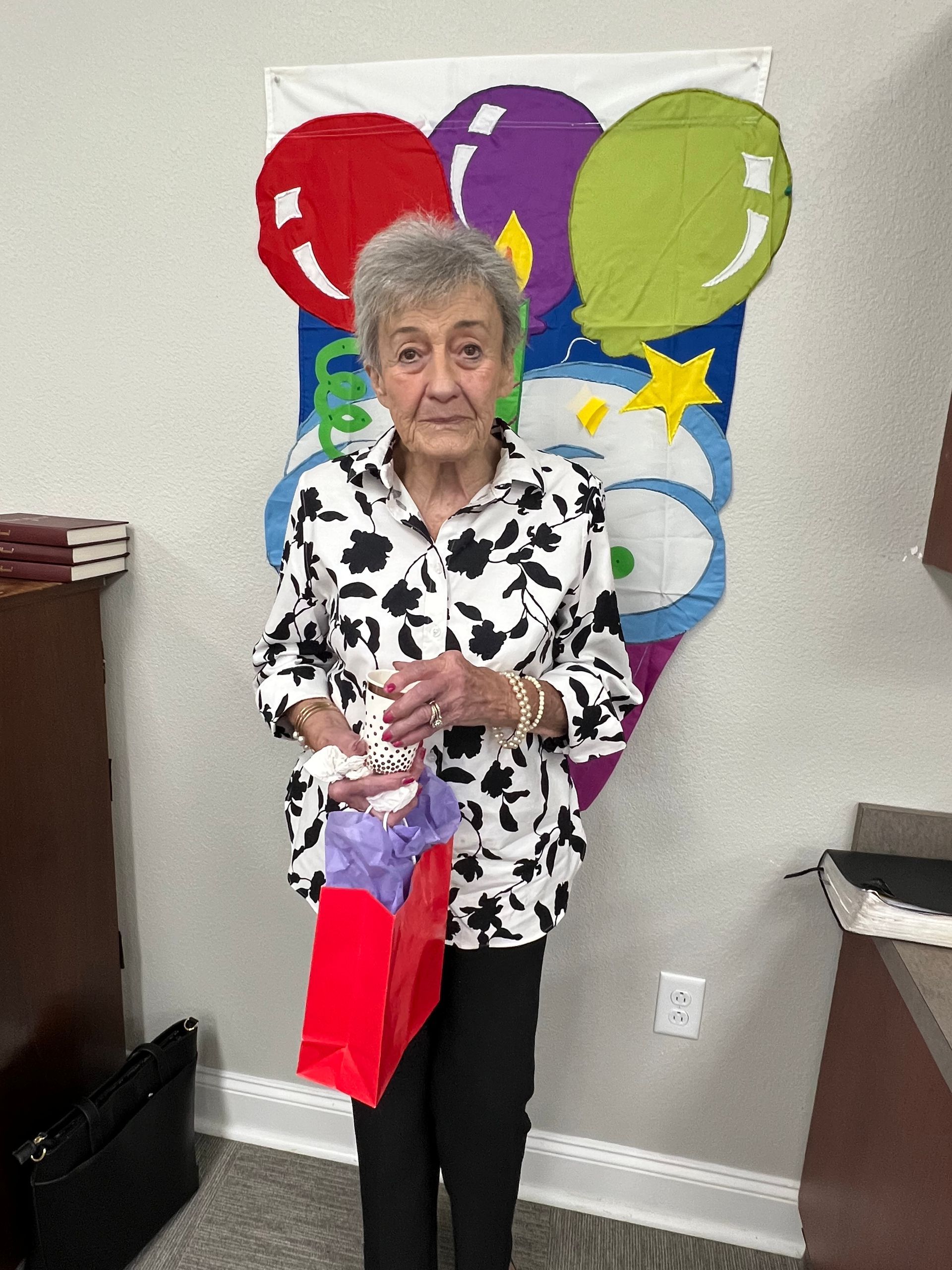 Woman holding a gift bag, standing in front of a birthday balloon banner.